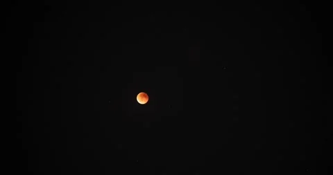 Timelapse of a lunar eclipse with the moon glowing in a reddish hue against a Stock Footage 316897666