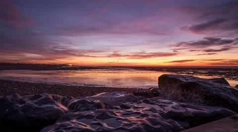 Timelapse of moving crimson clouds over rocky foreshore at sunrise. 스톡 동영상 59412091