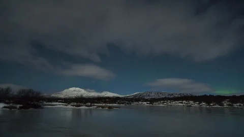Timelapse of northern lights and clouds moving over lake and snowy mountains Video stock 73011690