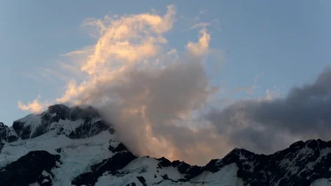 Timelapse of orange clouds backlit by sunset over dark snowy mountain range Stock Footage 74940540