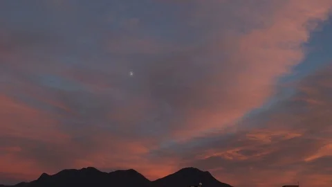 Timelapse of red clouds at sunset with mountains in the background and moon Stock Footage 121485887