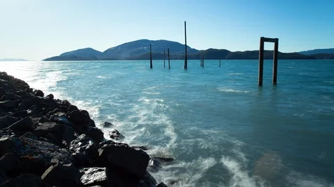 Timelapse of restless lake washing over stones with swaying waves on sunny day Stock Footage 129115060