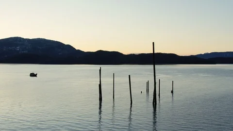 Timelapse of small motorboat floating around wooden pillars sticking out of lake Stock Footage 129113850