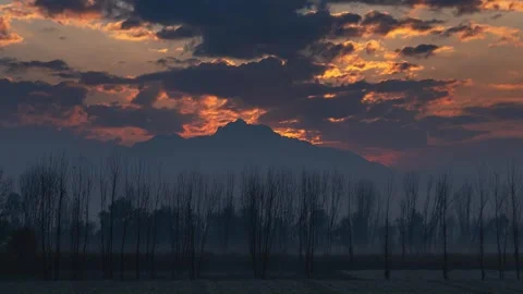 Timelapse of Sun Glowing behind Jagged Mountain Peak with Misty Trees Silhouette 스톡 동영상 332600359