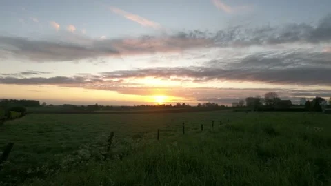 Timelapse of the sun rising over a grass field with a town in the distance a Stock Footage