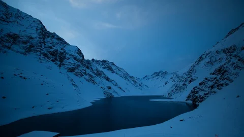 Timelapse of sun setting behind tall snow covered mountains as clouds pass by Stock Footage 124239341