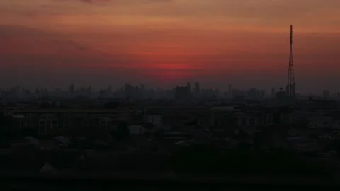 A timelapse of the sun setting over a sprawling city skyline. A tall cell tower Stock Footage 312109380