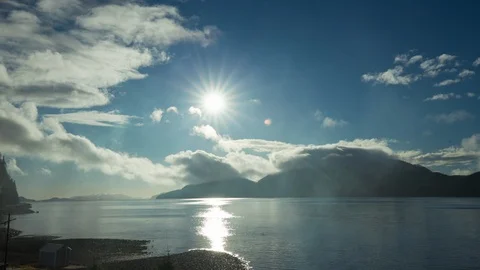 Timelapse of sun shining bright above lake with clouds passing over quickly Stock Footage 129114675