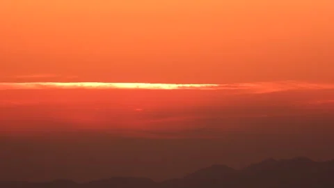 Timelapse sunrise emerges beneath thin clouds above dark mountain silhouettes Stock Footage 339935415