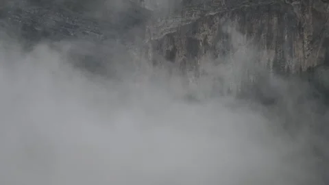 Timelapse swirling light gray clouds and mist moving in front of rugged Stock Footage 333074877