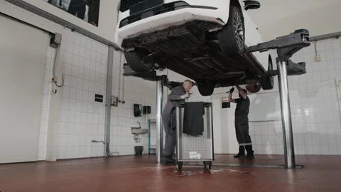 Timelapse of Two Mechanics Servicing Car on Hydraulic Lift in Garage Stock Footage 329433751