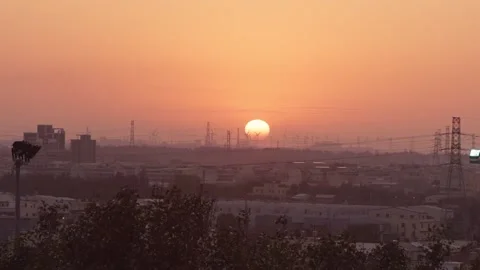 Timelapse of vibrant orange sun setting behind wind turbines under a cloudy sky Stock Footage 313497685
