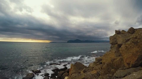 Timelapse waves hit the stone shore and overcast skies move to viewer in front Stock Footage 98176129