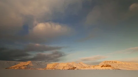 Timelapse of white clouds rolling over snow covered mountain ranges at sunset Stock Footage 73011763