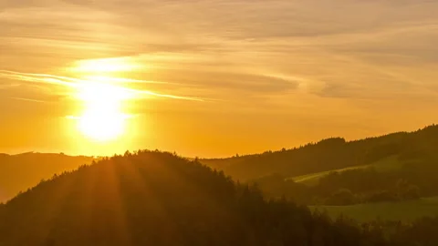 Timelapse zoomed by the setting sun over the top of a wooded hill shining Stock Footage 145618126