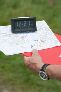 A timing clock is on a map attached to a clipboard held by a hand with watch Foto stock