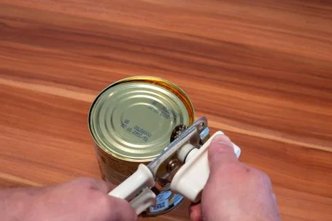 A tin can is opened with the help of a can opener Stock Photos