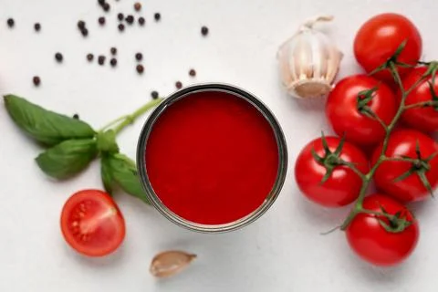 Tin can of tasty tomato paste with garlic, peppercorns and basil leaves on wh Stock Photos