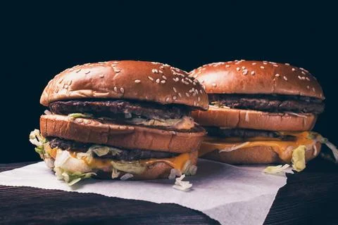 Tinted image two craft beef burgers on wooden table isolated on black backgro Stock Photos