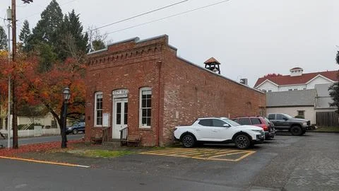 A tiny aged brick City Hall stands quietly beside an autumn-lined lot Stock Photos