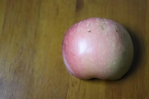 A Tiny Ant Crawling on a Fresh Pink Apple on a Wooden Surface Foto stock
