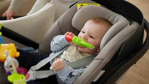 A tiny baby is sitting in a stroller and gnawing on a toy Video stock 239269770