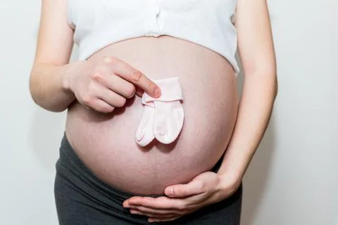 Tiny baby socks against the background of a pregnant belly, pink socks Stock Photos