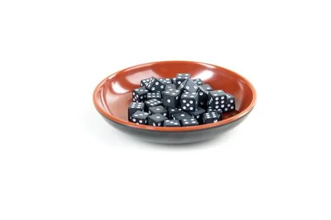 Tiny black and white dice pile in a red bowl isolated over white Stock Photos