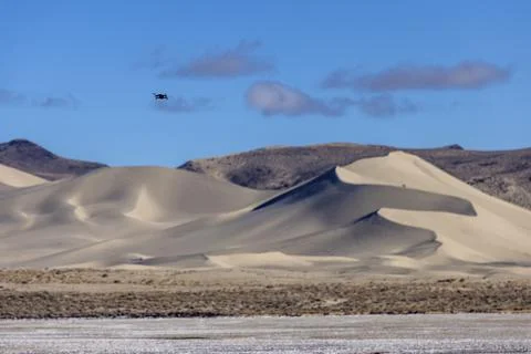 Tiny black drone flies towards sand dunes of Sand Mountain OHV park on a clea Stock Photos