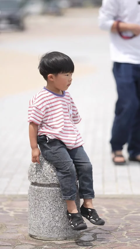 Tiny boy sits atop stone pillar, gazing thoughtfully Stock Footage 339831718