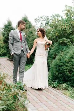 Tiny bride and groom in grey bouquet walk along the path Фото