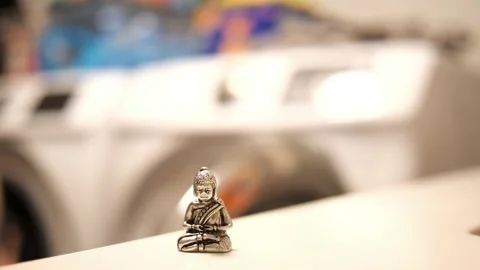 Tiny Buddha in focus with a man in the background doing various house chores Vidéo 278482820