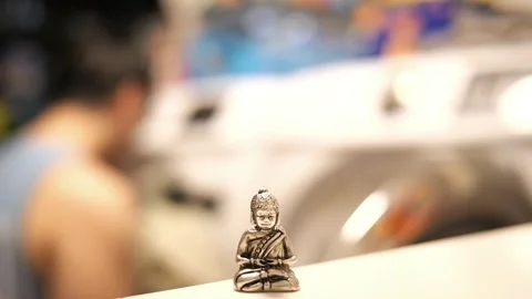 Tiny Buddha in focus with a man in the background doing various house chores Vidéo 278482849