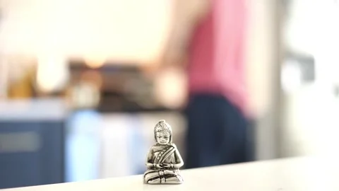 Tiny Buddha in focus with a man in the background doing various house chores Vidéo 278544259