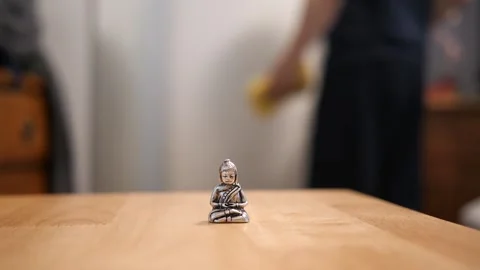 Tiny Buddha in focus with a man in the background doing various house chores Vidéo 278544263