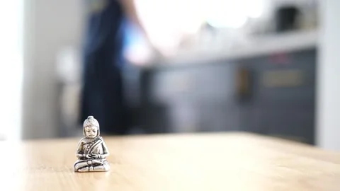 Tiny Buddha in focus with a man in the background doing various house chores Vidéo 278544279