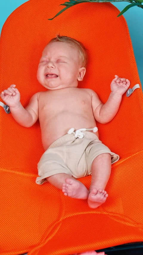 Tiny Caucasian infant lying in the baby chair starting to cry.  Stockbeeldmateriaal 304506491