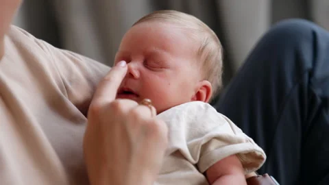 Tiny Caucasian infant sleeping in mom’s arms holding little fist at his cheek Stock Footage 250575215