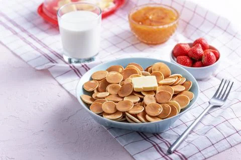 Tiny cereal pancakes with slice of butter, strawberries, honey and glass of m Stock Photos