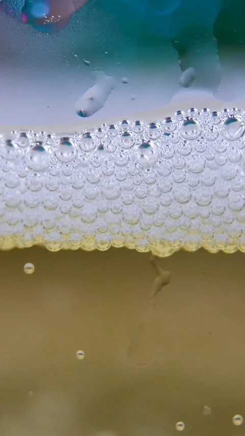 Tiny champagne bubbles ascend, creating sparkling effect with foam forming on Stock Footage 313906135