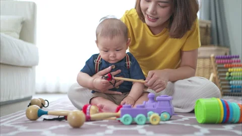 A tiny child cheerfully plays with toys on the floor with mom Stock Footage 287971359