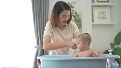A tiny child enjoys taking a bath in a baby bathtub with mom Stock Footage 289281168