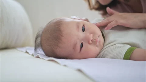 A tiny child smiles happily on the bed and mother is using a cotton bud Stock Footage 288006160