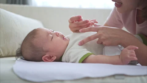 A tiny child smiles happily on the bed and mother is using a cotton bud Stock Footage 288006161