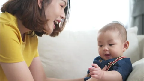 A tiny child smiling happily on the couch in the living room with mom Vídeos de archivo 287965594