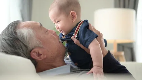 A tiny child smiling happily on the couch in the living room with grandfather Stock Footage 287975919