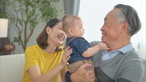 A tiny child smiling happily on the couch with mom and grandfather Stock Footage 287977436