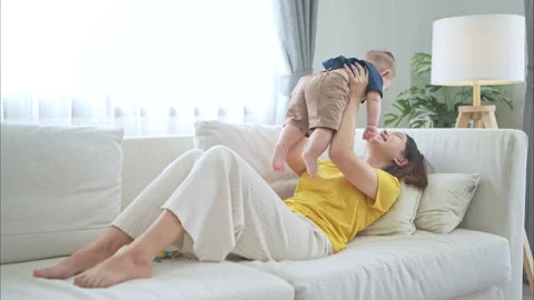 A tiny child smiling happily on the couch in the living room with mom Stock Footage 288001593