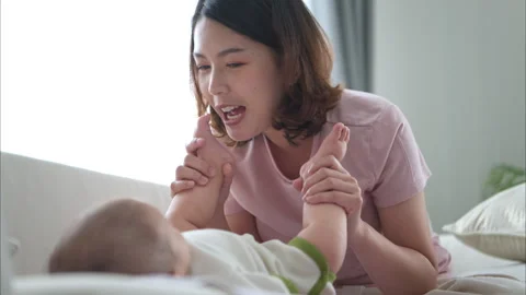 A tiny child smiling happily on the couch in the living room with mom Stock Footage 288003562