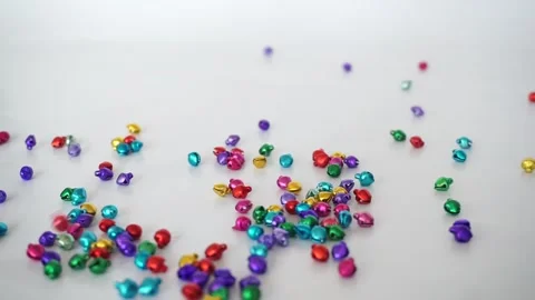 Tiny colourful jingle bells falling onto white surface Stock Footage 146664706